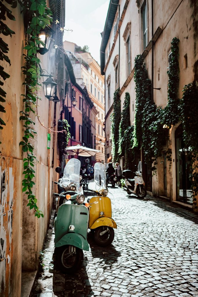 Narrow cobblestone street in Rome with parked scooters, old buildings, and ivy-covered walls in soft daylight