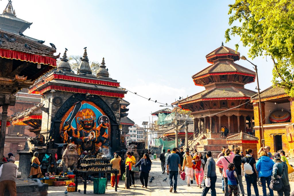 Kathmandu Durbar Square in Nepal, with a pagoda temple and a Bhairav shrine mural in a busy courtyard.