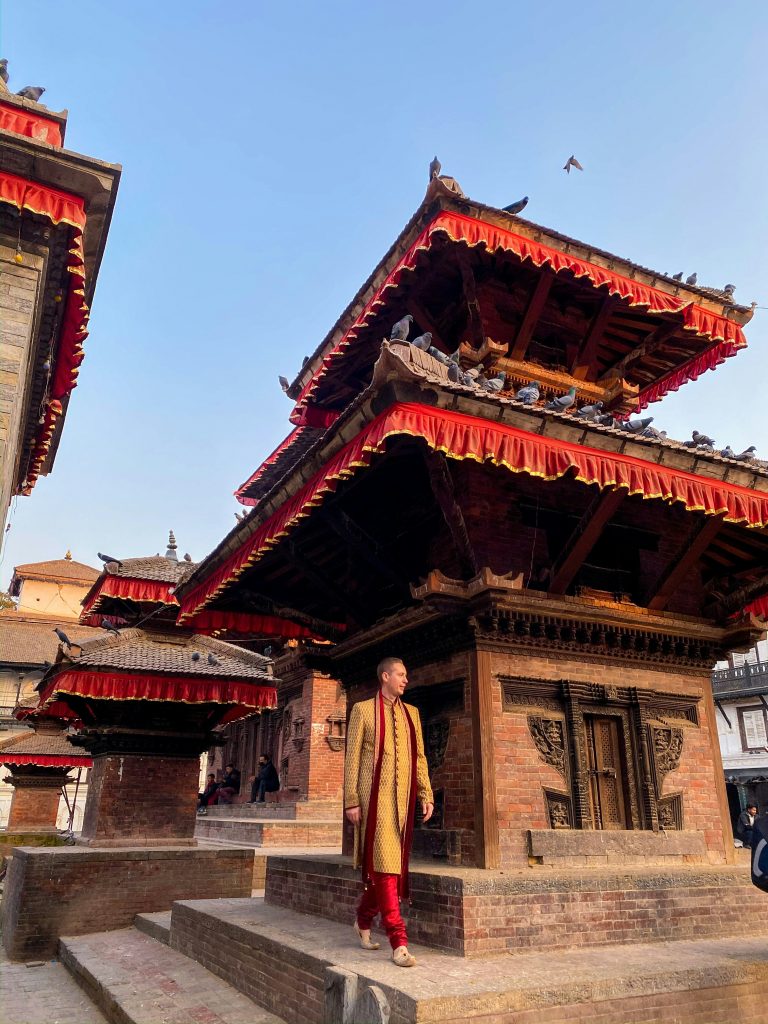 Pagoda-style temple in Kathmandu, Nepal, with carved wooden details and red eaves, as a visitor walks past.