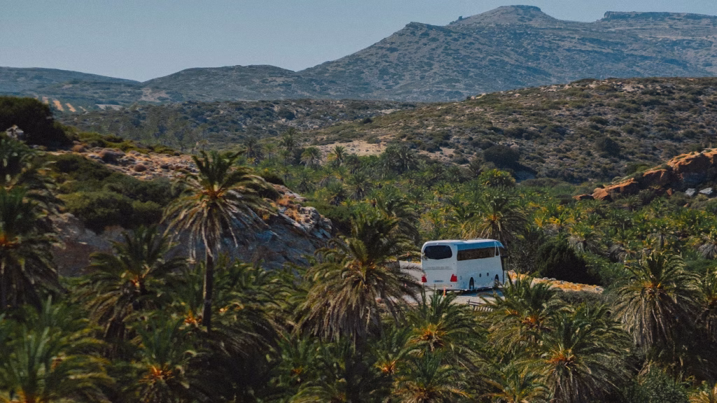 Intercity bus driving through palm valley in Crete with mountains in the background