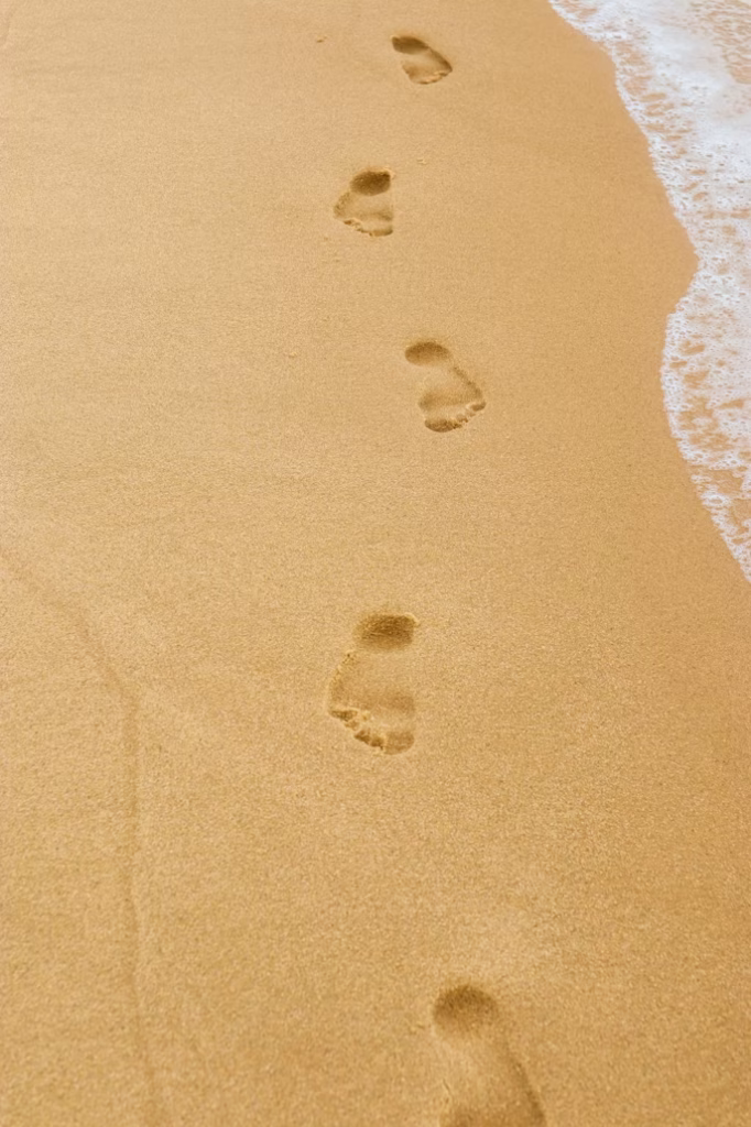 Footprints in soft sand near ocean waves