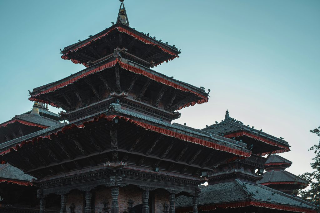 Traditional multi-tier pagoda temple in Nepal with carved wooden eaves and red trim against a clear sky.