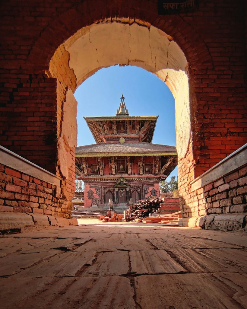 Changu Narayan Temple in Nepal framed by a brick archway, with carved wooden pagoda architecture.